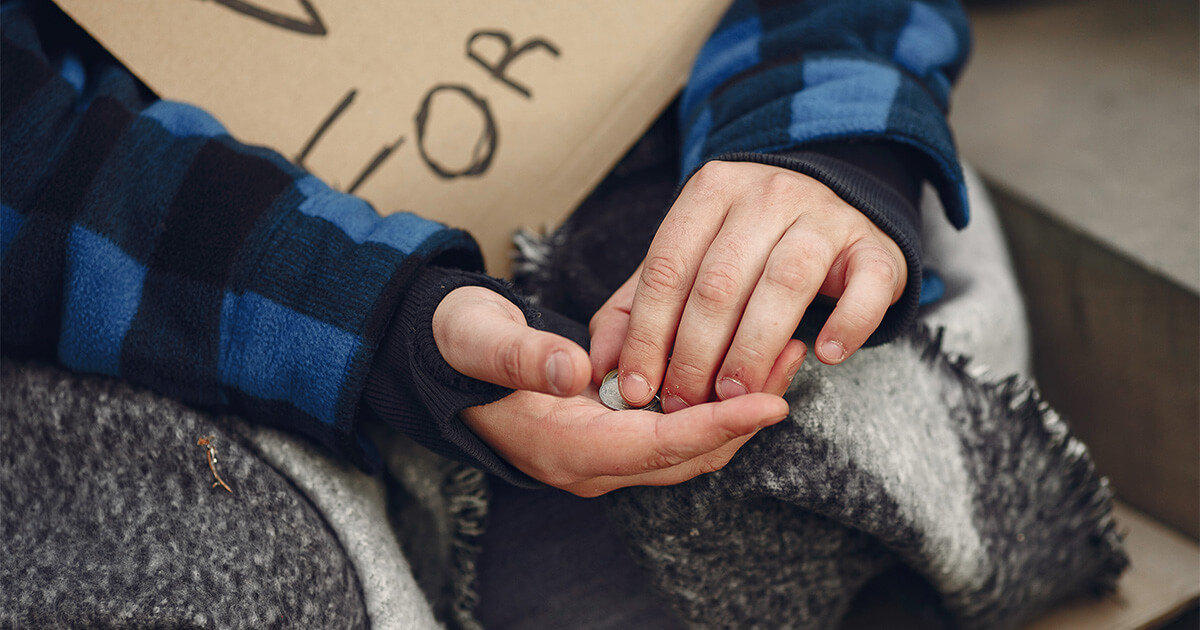 Homeless man with blanket on lap holding spare change.